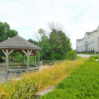 A scenic view featuring a gazebo by a path, surrounded by lush greenery and residential buildings in the background.