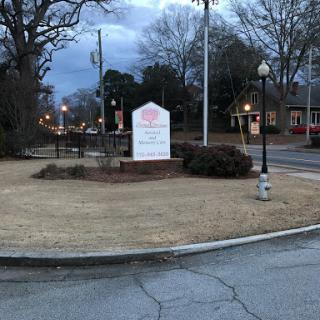 A park area with a sign illuminated in the evening light, surrounded by trees and street lamps.