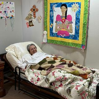 A person is lying in a bed with a colorful quilt on the wall and various room decorations.