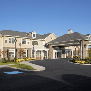 A large residential building with a landscaped entrance and driveway under a clear blue sky.