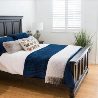 A cozy bedroom with a dark wooden bed frame, blue and white bedding, decorative pillows, and an indoor plant next to a window with shutters.