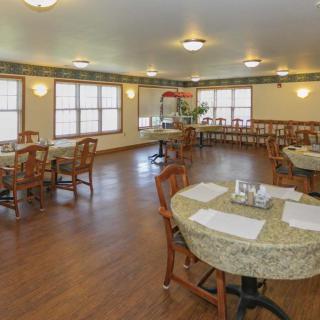 A spacious dining room with wooden floors, neatly arranged tables and chairs, and ample lighting.
