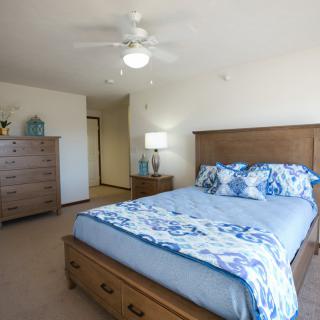 A cozy bedroom featuring a wooden bed frame, dresser, and a ceiling fan.
