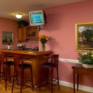 A cozy home bar setup with wooden furniture, pink walls, and decorative elements like flowers and paintings.