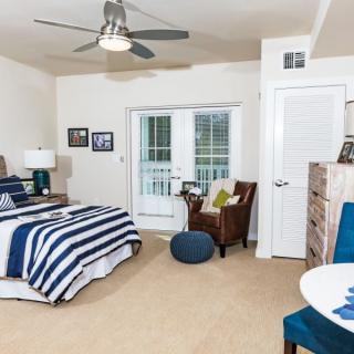 A cozy bedroom with striped bedding, featuring a ceiling fan and an armchair near a door and window.