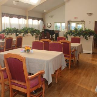 A well-lit dining room with neatly arranged tables and chairs, decorated with plants and natural lighting.