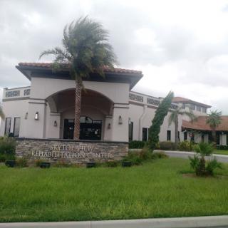 A modern architectural building surrounded by greenery and palm trees under a cloudy sky.