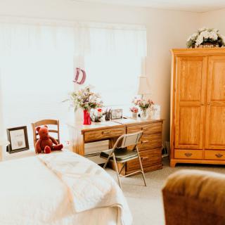 A cozy bedroom with warm wooden furniture, a comfortable bed, and natural light streaming in through the window.