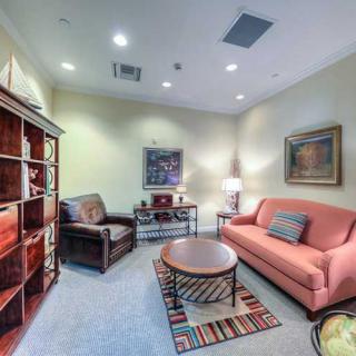 A cozy and well-lit living room with a pink sofa, armchair, bookshelf, and coffee table.