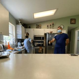 Two people wearing masks are in a kitchen, possibly preparing food.