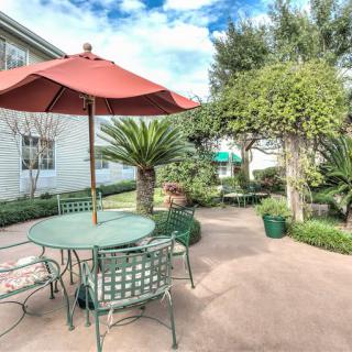 A serene patio with a table, chairs, and umbrella surrounded by lush greenery.