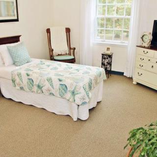 A cozy bedroom with a single bed adorned with floral bedding, a dresser, and a window letting in natural light.