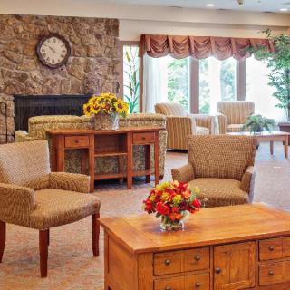 A cozy living room with comfortable chairs, a wooden coffee table adorned with flowers, and a stone fireplace.