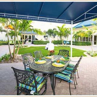 A cozy outdoor patio with a set dining table under a blue umbrella, surrounded by lush tropical greenery.