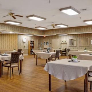 An empty dining room with neatly arranged tables and chairs, featuring wood flooring and elegant lighting.