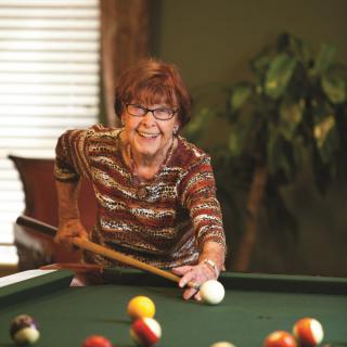 An elderly woman playing pool indoors with a focused expression.