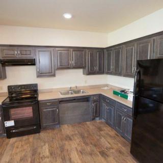 A modern kitchen with dark cabinets, appliances, and wooden flooring.