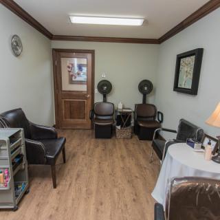 A small waiting area in a hair salon with chairs, magazines, and hair drying equipment.