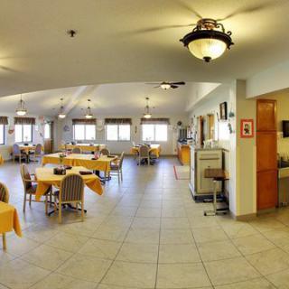 A spacious dining room with neatly arranged tables and chairs, featuring large windows and warm lighting.