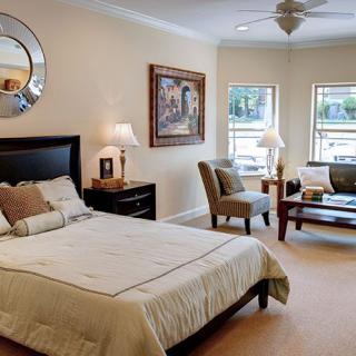A cozy bedroom with a bed, chairs, and large windows allowing natural light.