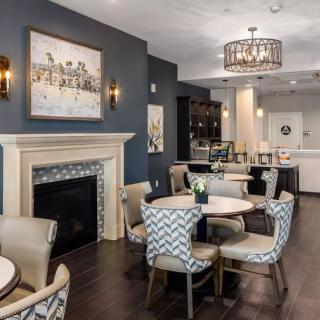 A modern dining area featuring a cozy fireplace, elegant chandelier, and stylish upholstered chairs around round tables.