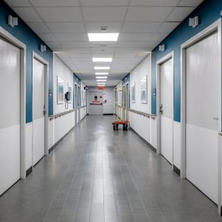 A view down an empty hospital corridor with white doors and blue walls.