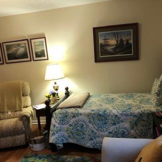 A cozy living room with a bed, reclining chair, lamp, and wall art.