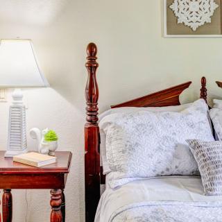 A cozy bedroom with a wooden bed, floral bedding, and a bedside table featuring a lamp and decorative items.