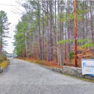 A gravel road lined with tall trees and a sign on the right side.