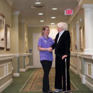 A caregiver engaging in a warm conversation with an elderly individual in a well-lit hallway.