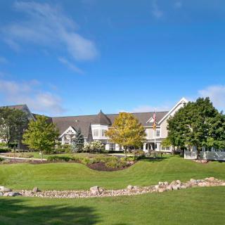 A luxurious house with a well-maintained garden and trees under a clear blue sky.
