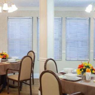 A well-lit dining room with neatly arranged tables and chairs, decorated with flowers and set for a meal.
