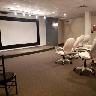 A conference room equipped with comfortable chairs and a large projector screen.