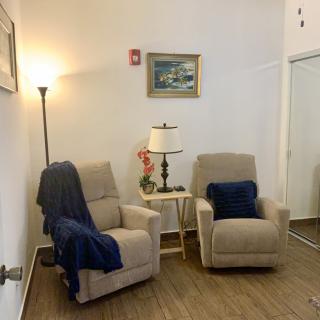 A cozy living room corner with two beige recliner chairs, a floor lamp, and a small table adorned with a table lamp and decor.