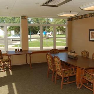 A bright meeting room with a large table and several chairs, illuminated by natural light through large windows.