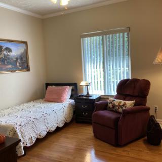 A cozy bedroom with a single bed, an armchair, and a lamp beside a window.