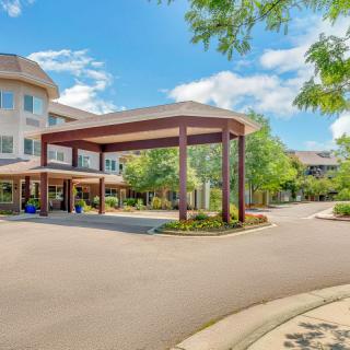 A sunny exterior view of a building entrance with a covered driveway and landscaped surroundings.
