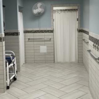 A hospital corridor with a wheelchair, tiled walls and floor, handrails, and a door at the end.