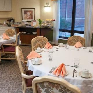 A neatly arranged dining room with tables set for a meal, featuring folded napkins and complete tableware.