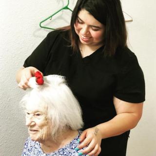 A caregiver is styling the hair of an elderly woman, showcasing a moment of personal care and attention.