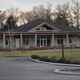 A modern building with a large front yard, surrounded by trees and a parking lot.