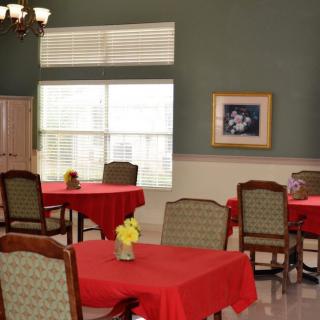 A dining room with tables covered in red tablecloths and chairs, featuring a large window and framed wall art.