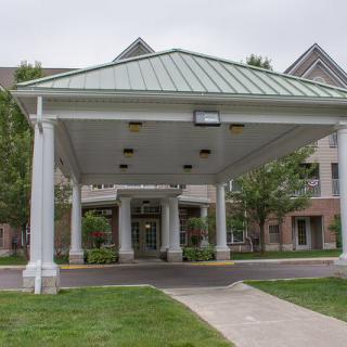 A building entrance with a large canopy supported by columns and a concrete pathway leading to the doors.