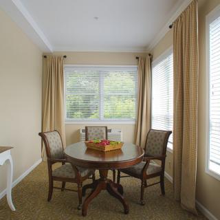 A cozy dining area with a round table and chairs by large windows with beige curtains.