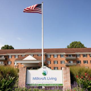 An apartment building with a prominently displayed American flag and a sign reading 'Milcroft Living' in front, surrounded by well-maintained landscaping.