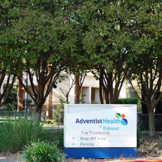A sign outside AdventHealth, surrounded by greenery.