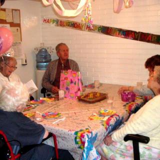 A group of seniors celebrating a birthday with decorations and gifts around a table.