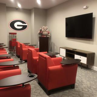 A sports-themed media room featuring red chairs and a large television.