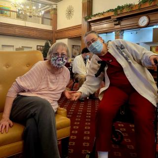 Two women wearing masks sitting together in a nursing home.