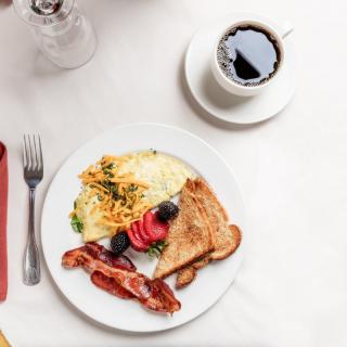 A delicious breakfast plate with scrambled eggs, bacon, toast, and a cup of coffee.